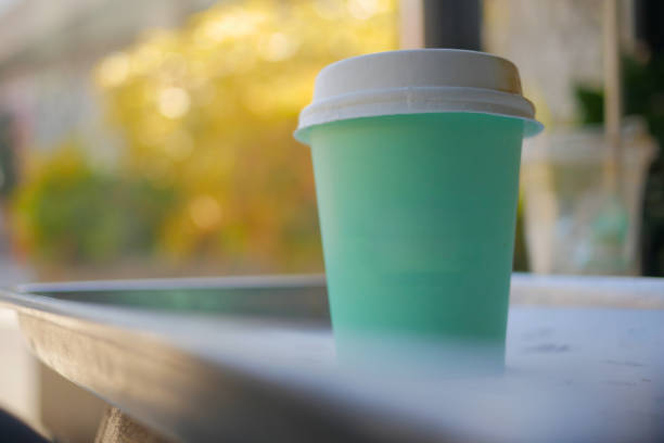 A stylish mint green disposable coffee cup sitting outdoors, blurred background.