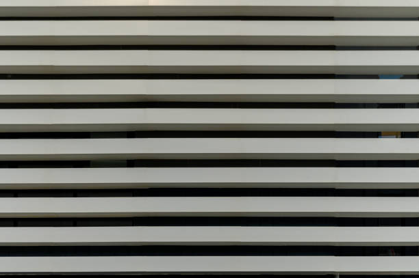 Vertical lines converge as sleek white slats create a rhythmic pattern on a modern urban structure during daylight.