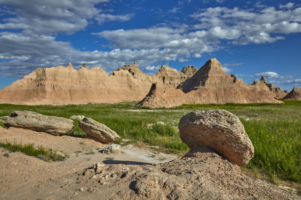 Panoramic view of eroded rock formations in Badlands National Park, South Dakota. Rugged buttes rise from the grassy prairie under a dramatic blue sky with dark clouds