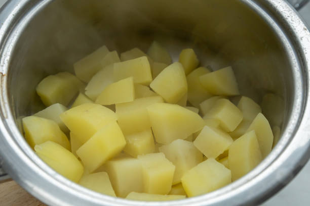 The boiled potatoes are nestled in a stainless steel pot, perfectly cooked and ready to be served. The close-up shot captures the soft texture and smooth surface of the potatoes.