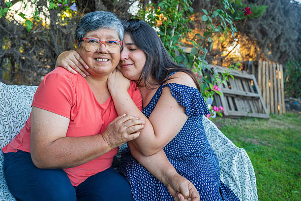 Two women sit together on a couch, hugging each other affectionately