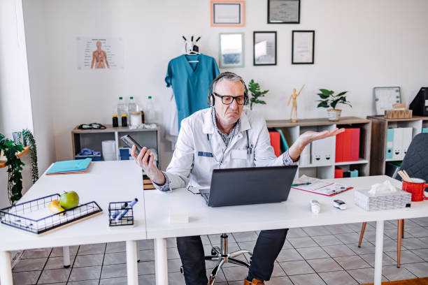 Doctor trying to catch up with work while being alone office and using mobile phone