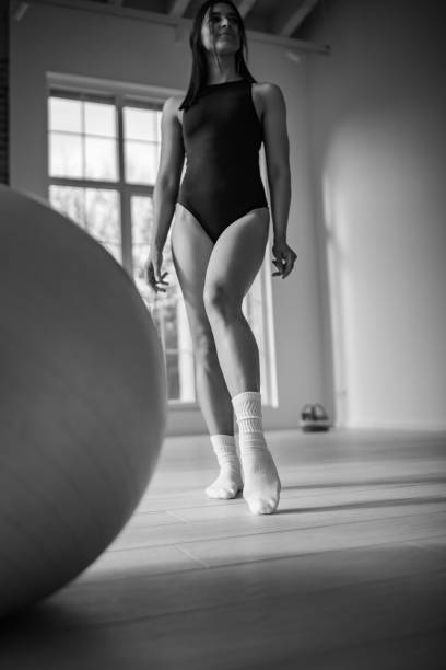A young woman is engaged in a pilates session in a spacious indoor studio, showcasing her concentration and flexibility as she utilizes equipment for her workout routine.