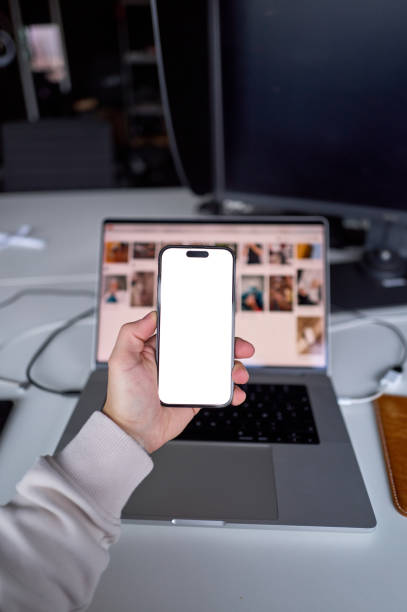 istock Designer holding smartphone with white screen mockup over laptop in home office 2201144636