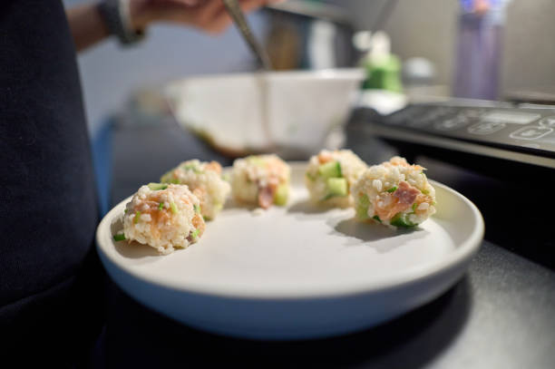 Close-up of a chef preparing delicious salmon and cucumber sushi balls on a white plate in a kitchen setting