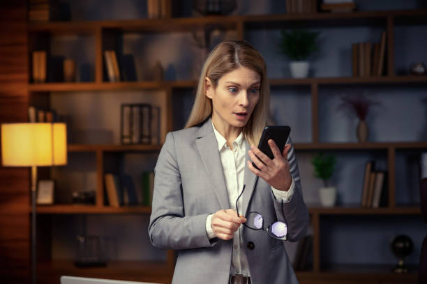istock Surprised young woman makes big eyes opens, shocked with unprecedentedly notification or message, looking at mobile phone, working at home office. 2201149496