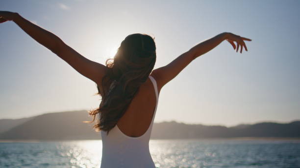 istock Woman stretching sunlight beach wearing white swimsuit back view. Slim brunette 2201152840