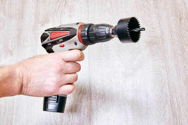Hand holds cordless drill with hole saw attachment.