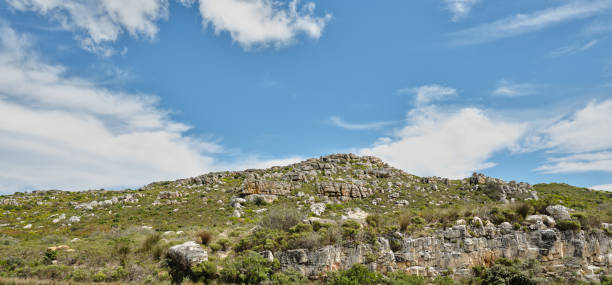 A scenic view featuring a rocky terrain covered with low vegetation, set against a bright blue sky adorned with white, scattered clouds, representing natural beauty and tranquility in a serene environment.