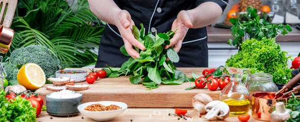 istock Chef blogger holds fresh spinach in hands Cozy kitchen with wooden table, kitchenware, vegetables, herbs and ingredients for cooking. Healthy vegan food, eating, culinary, recipes, blogging 2201167384