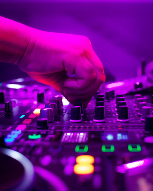 A DJ mixing on a board in a club environment. purple lights are illuminating the mixer