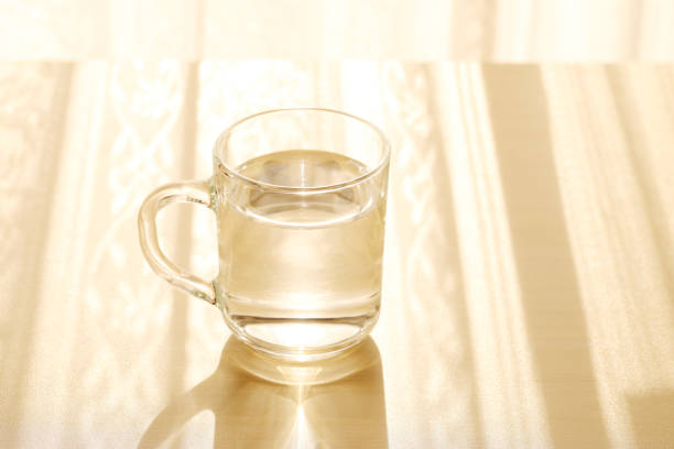 glass cup of water on a wooden table with the morning sun shining on the background