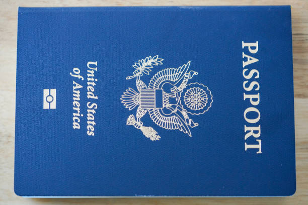 Clear image of a U.S. passport cover, featuring a deep blue background with the word 'PASSPORT' in white uppercase letters at the top. The cover displays the U.S. eagle emblem, the text 'United States of America,' and a small U.S. flag symbol at the bottom, all embossed in white. The passport is placed on a light wooden surface, adding a natural and textured contrast to the official document.