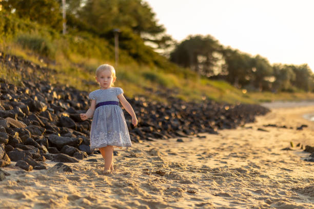 istock Child explores sandy beach while enjoying a warm sunset near rocky shoreline during summer evening 2201182740