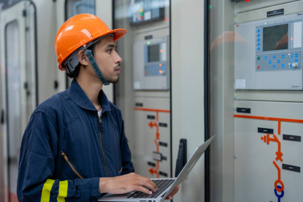 istock technician in orange helmet operates laptop near control panels in modern facility, showcasing focused and professional atmosphere 2201193920