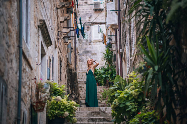 A mid adult woman in a green dress walks through the narrow streets of the old town in Dubrovnik, Croatia.