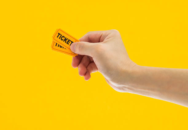 Hand holding two cinema tickets on yellow background