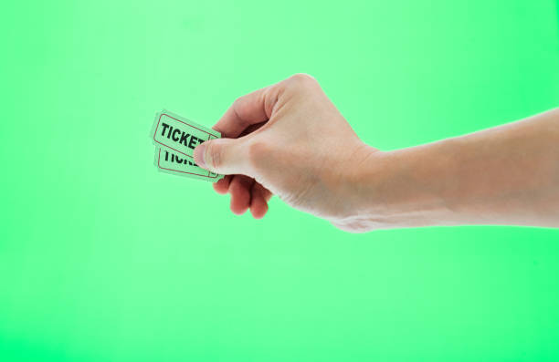 Hand holding two cinema tickets on green background