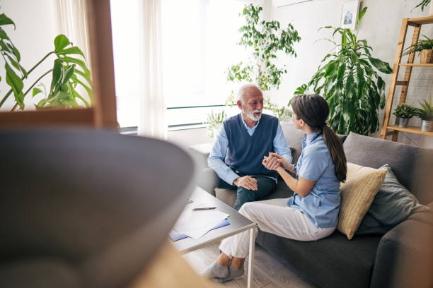 istock Nurse holding hand of senior man sitting on sofa, providing comfort and support 2201217090