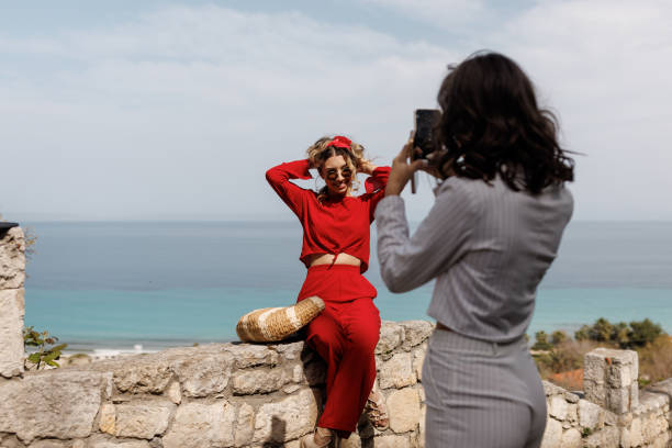 Young female friends taking photos on mobile phone during vacation at seaside