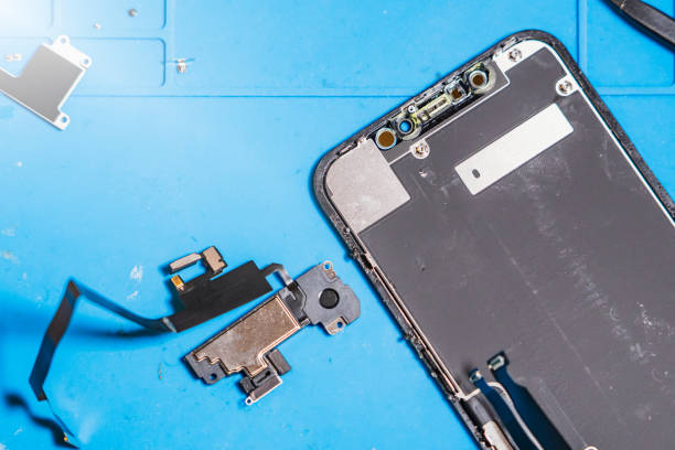 istock Expert phone repair in progress with broken parts on blue workbench and tools scattered around 2201221201