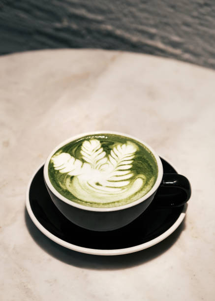 Matcha green tea latte with intricate latte art served in a black cup on a marble table, Japanese-inspired café beverage and modern coffee culture concept