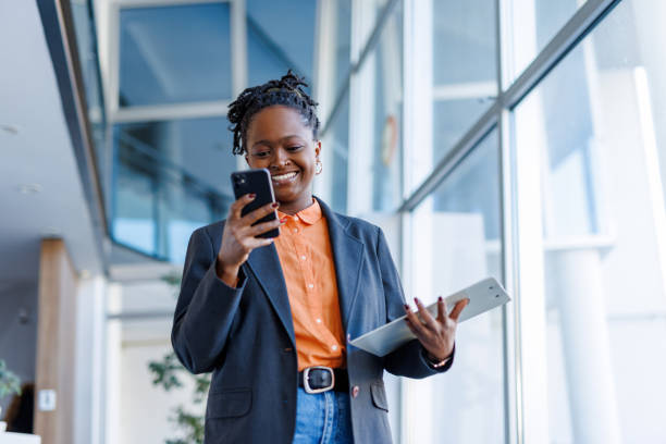 istock Smiling businesswoman using smartphone and holding clipboard in modern office 2201222267