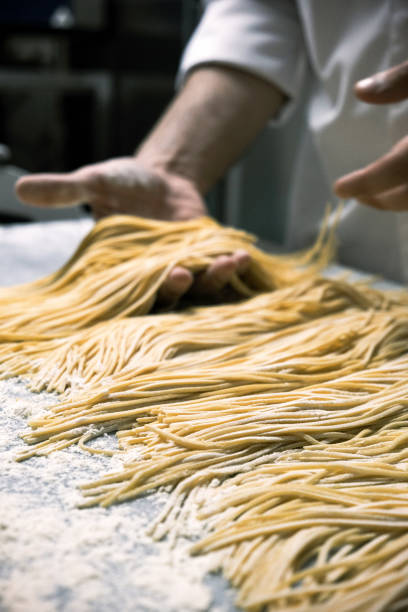 istock Close-up of a chef handling freshly made pasta strands on a floured surface, artisan pasta-making process in a professional kitchen setting 2201222900