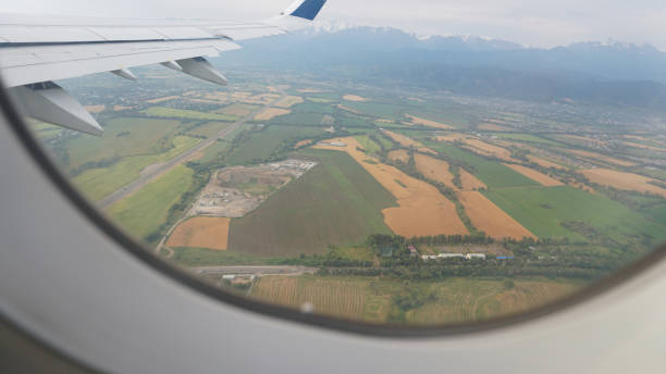 istock Airplane wing flying over agricultural landscape with mountains in background 2201235644