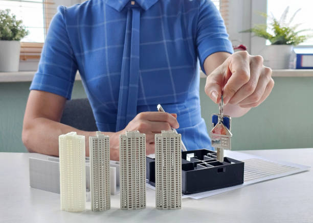 istock Real estate agent showcases miniature buildings while holding keys 2201237130