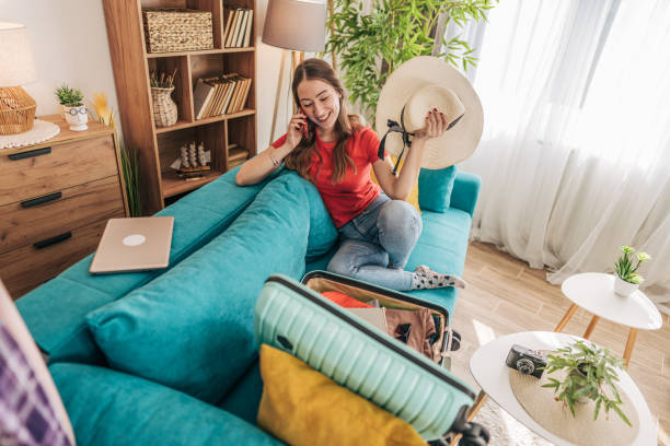 istock Young woman preparing suitcase for summer vacation while talking on phone 2201239061