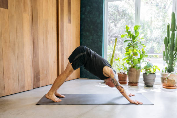 istock Senior man with tattoos practising yoga at home, downward dog 2201239368