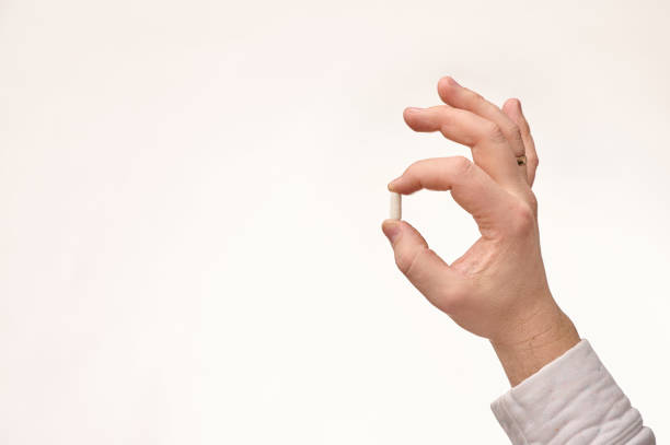 istock Hand holding a small white capsule against a neutral background, suggesting health or medication focus 2201241990
