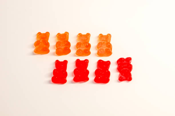 istock Eight multicolored gummy bears are arranged on a white background. The top four bears are orange, the bottom four are red. The bears stand evenly, equidistant from each other. 2201246449