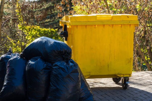 istock Bright yellow garbage bin stands next to piled black trash bags under clear blue skies in a lush green park setting 2201253746