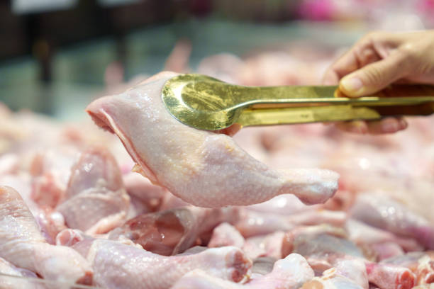 Close-up of a shopper using golden tongs to select fresh chicken pieces at a local market, showcasing freshness and ingredient quality.