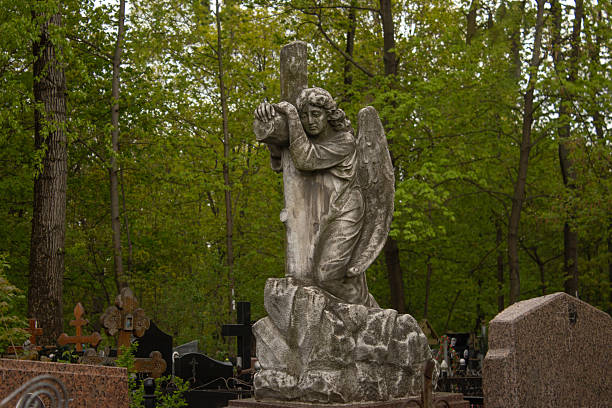 Statue of a melancholic female figure in front of a cross. Cloudy day, atmosphere of sadness.