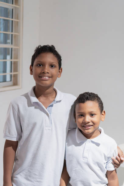 Two brothers are posing together, wearing white polo shirts, smiling and hugging