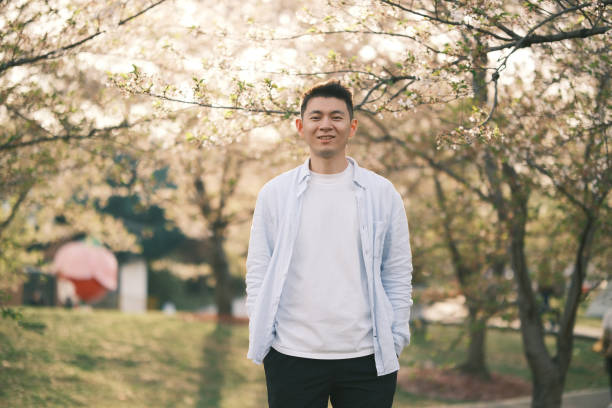 istock smiling handsome Asian young with sakura blossom tree, front view looking at camera 2201282145