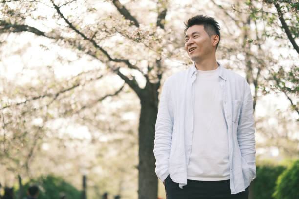 istock happy smiling Asian young man and sakura blossom tree 2201282163