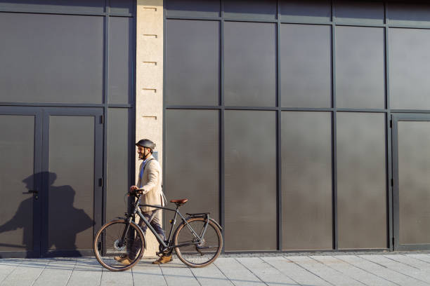 istock Professional man walking a bicycle past modern glass building exterior 2201291337
