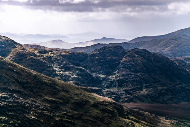 istock The image shows a mountainous region. Dark, rugged terrain dominates the foreground, contrasting with lighter, distant hills. 2201291404