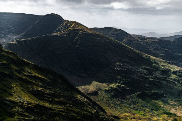 istock Steep, dark-colored hills and mountains are presented. The sky is light grey. 2201291406