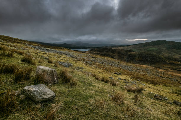Simple landscape with focus on a large rock in a field, distant hills, cloudy weather.