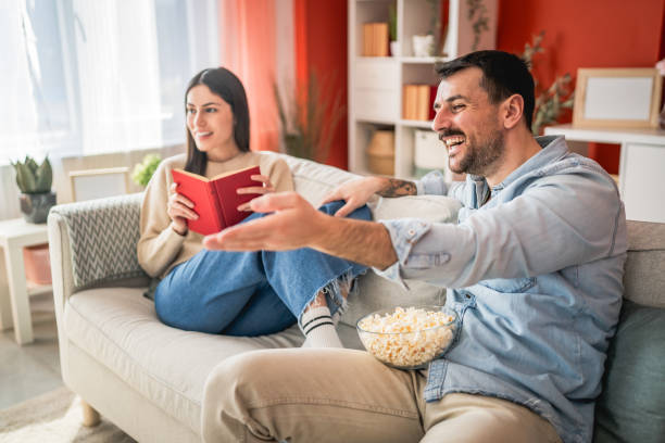 istock man sit on sofa watch movie and eat popcorn while woman read a book 2201298855