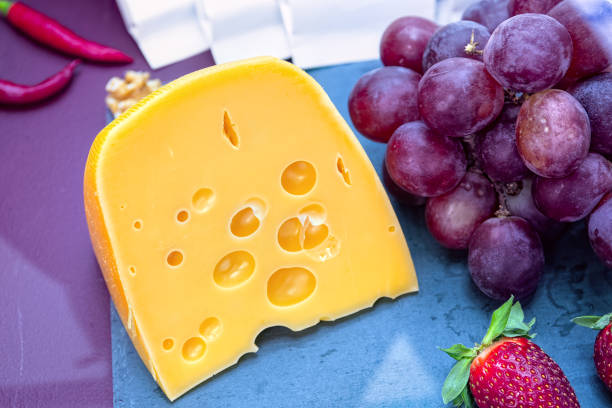 Piece of yellow cheese with grape and strawberries on blue background.