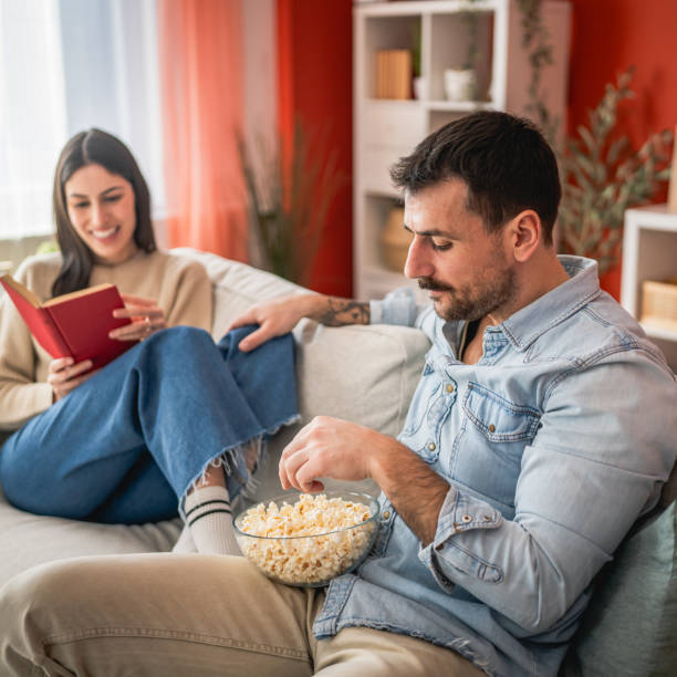 istock man sit on sofa watch movie and eat popcorn while woman read a book 2201298990