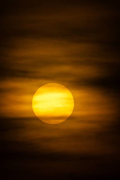 A dramatic sunset or sunrise with a large, golden sun shining through a layer of soft, blurred clouds, creating a warm, atmospheric mood.