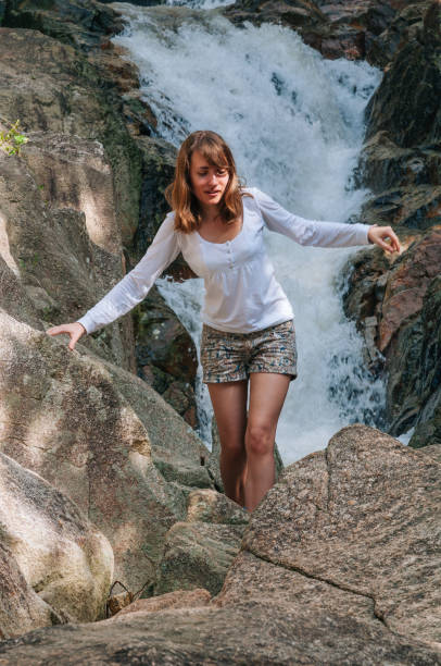 Young adult woman carefully navigating rocky terrain in front of a flowing waterfall