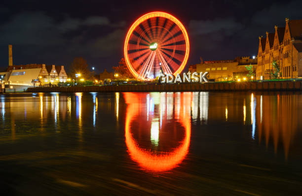 Long-exposure night shot of the red Devil's Wheel reflecting in water, with neon Gdask signage. Perfect for urban, travel, or neon-lit themes